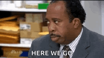 A Man In A Suit And Tie Is Saying `` Here We Go '' While Looking At Something . GIF