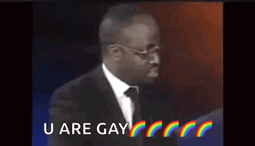 A Man In A Suit And Tie Is Saying `` U Are Gay '' With Rainbows In The Background . GIF