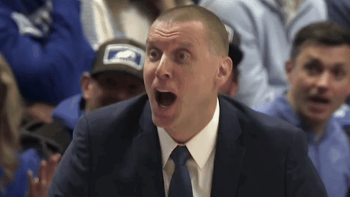 A Man In A Suit And Tie Is Screaming In Front Of A Crowd GIF