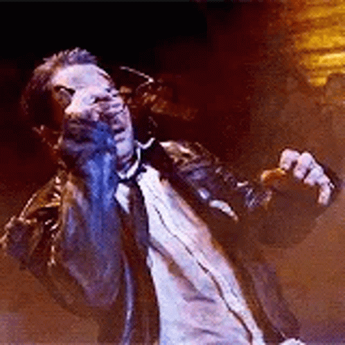 A Man In A Suit And Tie Is Singing Into A Microphone While Standing On A Stage . GIF