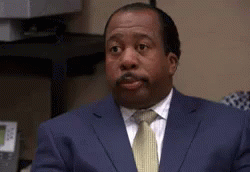 A Man In A Suit And Tie Is Sitting At A Desk And Making A Funny Face . GIF