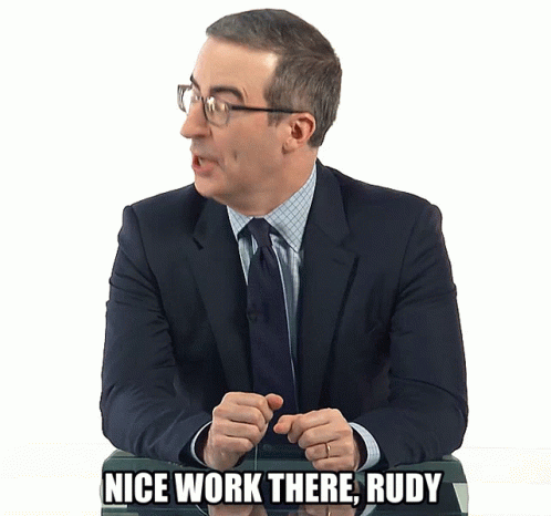 A Man In A Suit And Tie Is Sitting At A Desk And Says Nice Work There Rudy GIF