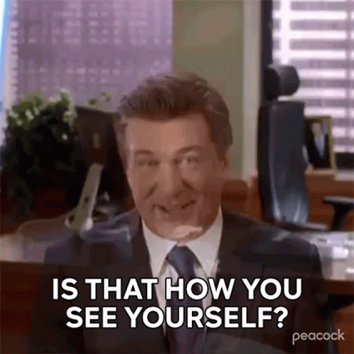 A Man In A Suit And Tie Is Sitting At A Desk And Smiling . GIF