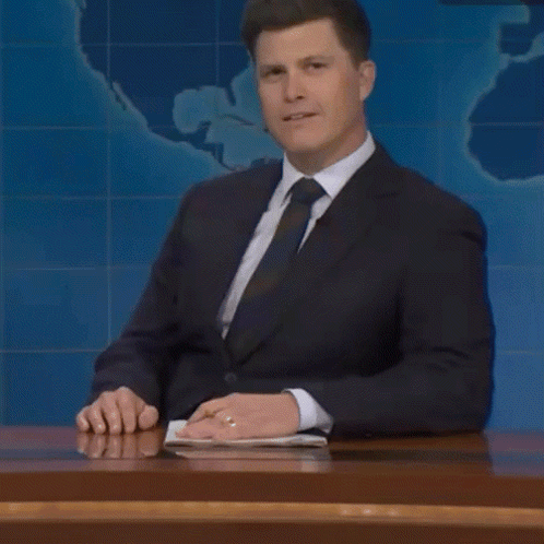 A Man In A Suit And Tie Is Sitting At A Desk And Talking About Something GIF