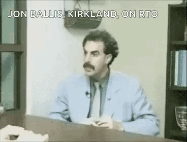 A Man In A Suit And Tie Is Sitting At A Desk And Talking . GIF