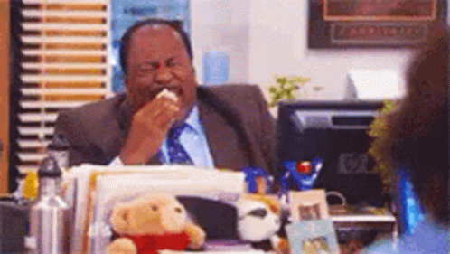 A Man In A Suit And Tie Is Sitting At A Desk Eating A Piece Of Bread . GIF