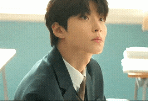 A Man In A Suit And Tie Is Sitting At A Desk In A Classroom . GIF