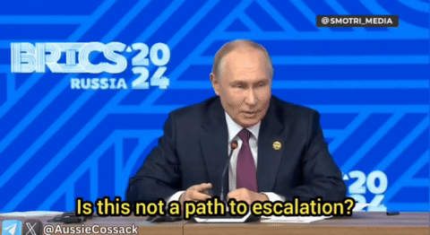 A Man In A Suit And Tie Is Sitting At A Desk In Front Of A Blue Background That Says Russia 24 GIF