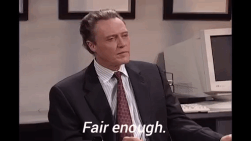 A Man In A Suit And Tie Is Sitting At A Desk In Front Of A Computer . GIF