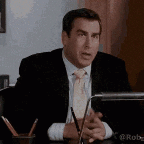 A Man In A Suit And Tie Is Sitting At A Desk In Front Of A Computer . GIF