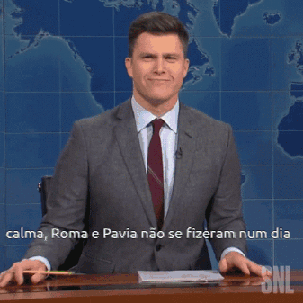 A Man In A Suit And Tie Is Sitting At A Desk In Front Of A Snl Sign GIF
