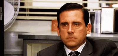 A Man In A Suit And Tie Is Sitting At A Desk In Front Of A Window . GIF