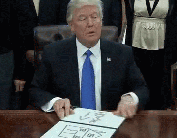 A Man In A Suit And Tie Is Sitting At A Desk With A Drawing Of A House On A Piece Of Paper . GIF