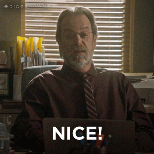 A Man In A Suit And Tie Is Sitting At A Desk With A Laptop And Says Nice GIF