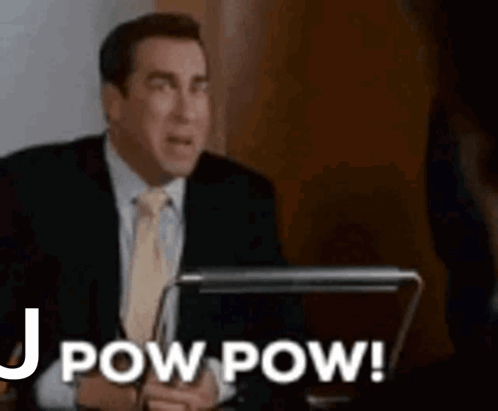 A Man In A Suit And Tie Is Sitting At A Desk With A Laptop And Says `` Pow Pow '' . GIF