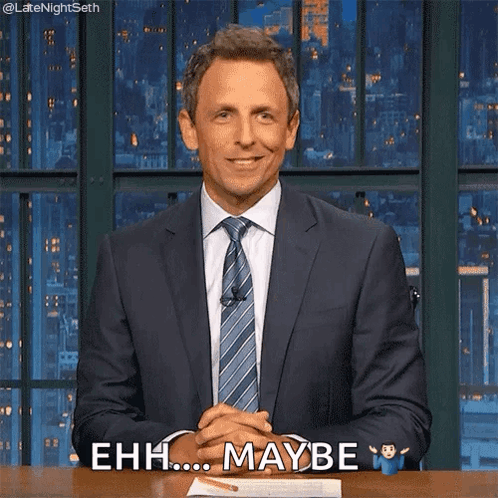 A Man In A Suit And Tie Is Sitting At A Desk With His Hands Folded And Says Ehh Maybe GIF
