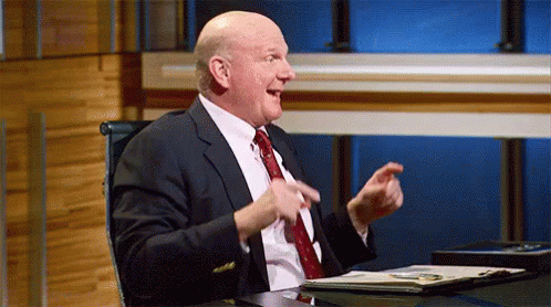 a man in a suit and tie is sitting at a desk with his hands in the air .