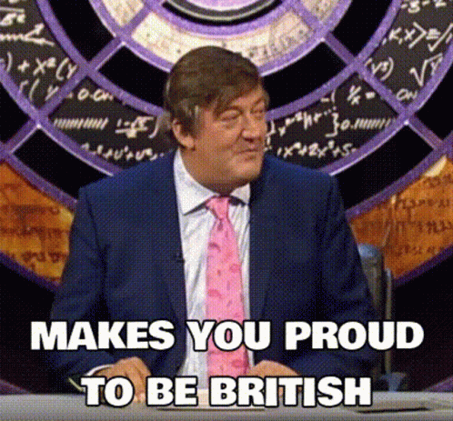 A Man In A Suit And Tie Is Sitting At A Desk With The Words Makes You Proud To Be British Below Him GIF