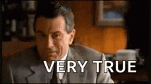 A Man In A Suit And Tie Is Sitting At A Desk With The Words `` Very True '' Written Above Him . GIF
