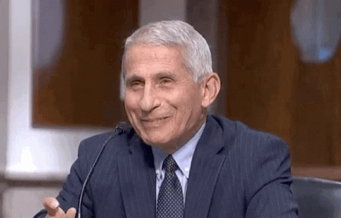 A Man In A Suit And Tie Is Sitting At A Microphone And Smiling . GIF