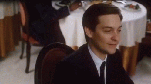 A Man In A Suit And Tie Is Sitting At A Restaurant Table . GIF
