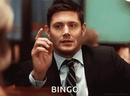 A Man In A Suit And Tie Is Sitting At A Table And Pointing Up With His Finger . GIF