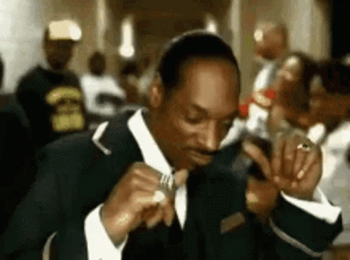 A Man In A Suit And Tie Is Sitting At A Table Eating A Sandwich . GIF
