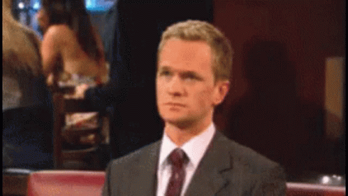 A Man In A Suit And Tie Is Sitting At A Table GIF