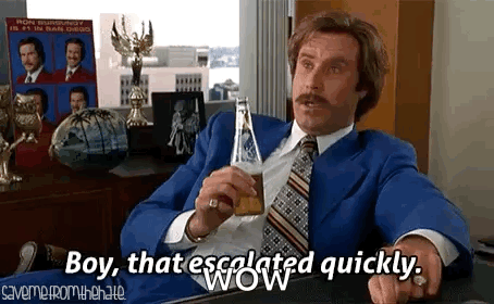 A Man In A Suit And Tie Is Sitting At A Table Holding A Bottle Of Beer . GIF