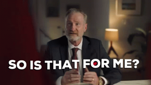 A Man In A Suit And Tie Is Sitting At A Table Holding A Cup Of Coffee And Talking . GIF