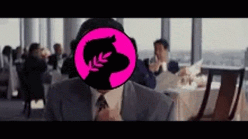 A Man In A Suit And Tie Is Sitting At A Table In A Restaurant With A Pink Circle On His Face . GIF