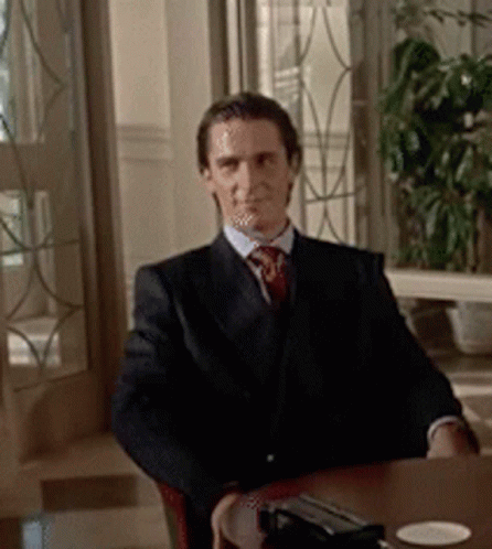 a man in a suit and tie is sitting at a table looking at the camera