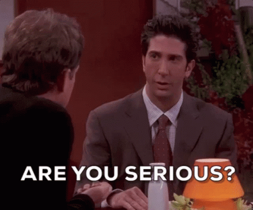 A Man In A Suit And Tie Is Sitting At A Table Talking To Another Man And Says Are You Serious . GIF