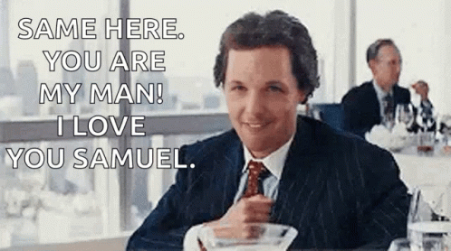 A Man In A Suit And Tie Is Sitting At A Table With A Bowl Of Food And A Glass Of Wine . GIF