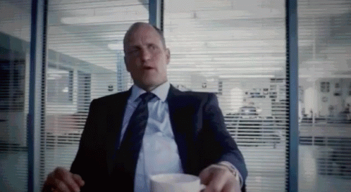 A Man In A Suit And Tie Is Sitting At A Table With A Cup Of Coffee . GIF