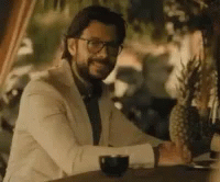 A Man In A Suit And Tie Is Sitting At A Table With A Glass Of Wine . GIF