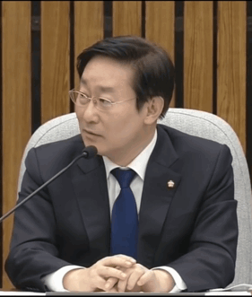 A Man In A Suit And Tie Is Sitting At A Table With A Microphone GIF