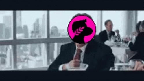 A Man In A Suit And Tie Is Sitting At A Table With A Pink Circle In Front Of His Head . GIF