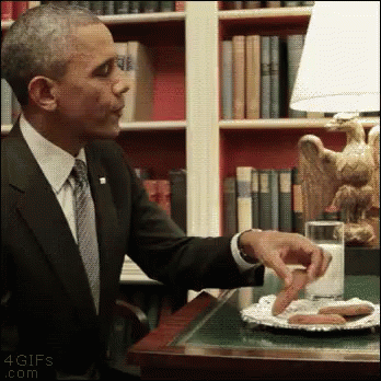 A Man In A Suit And Tie Is Sitting At A Table With A Plate Of Sausages And A Glass Of Milk GIF