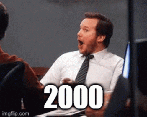 A Man In A Suit And Tie Is Sitting At A Table With A Surprised Look On His Face And The Number 2000 Written On The Scree GIF