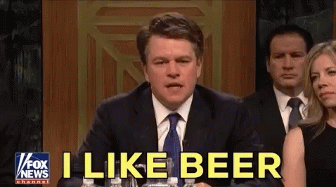 A Man In A Suit And Tie Is Sitting At A Table With Bottles Of Water And Says I Like Beer . GIF