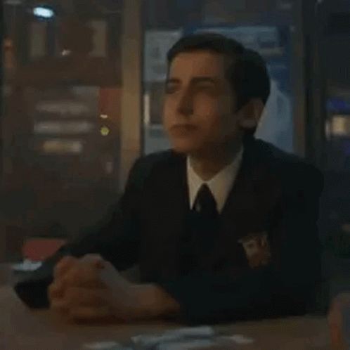 A Man In A Suit And Tie Is Sitting At A Table With His Hands Folded In Prayer . GIF