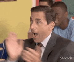 A Man In A Suit And Tie Is Sitting At A Table With His Hands In The Air And His Mouth Open . GIF