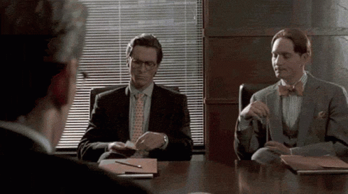 a man in a suit and tie is sitting at a table with other men .