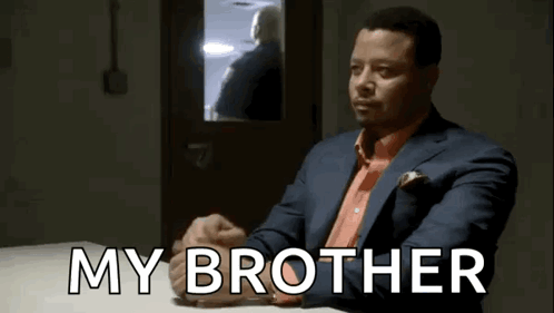 A Man In A Suit And Tie Is Sitting At A Table With The Words My Brother Written On It . GIF