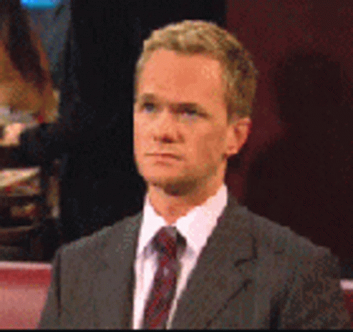 A Man In A Suit And Tie Is Sitting Down GIF