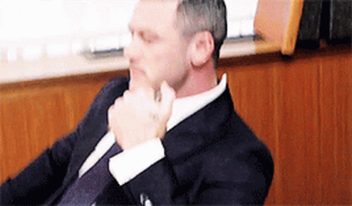 A Man In A Suit And Tie Is Sitting In A Chair . GIF