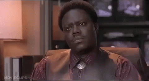 A Man In A Suit And Tie Is Sitting In A Chair And Looking At The Camera . GIF