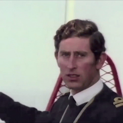 A Man In A Suit And Tie Is Sitting In A Chair And Looking At The Camera . GIF