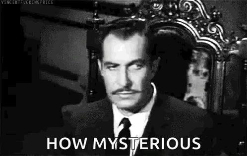 A Man In A Suit And Tie Is Sitting In A Chair And Looking At The Camera . GIF